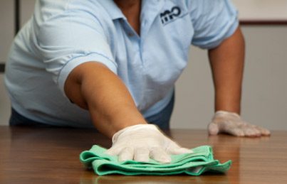 Woman providing office cleaning services by wiping a conference room table surface